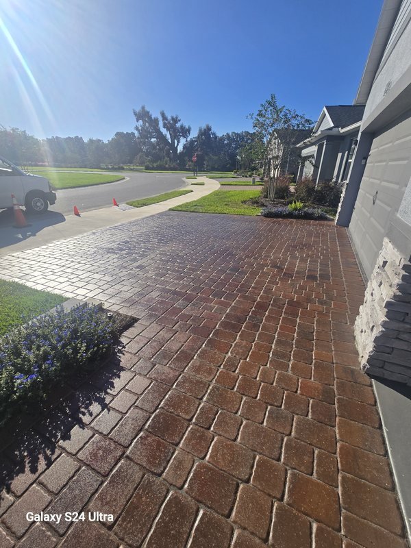 Stamped and stained brick-pattern driveway leading to a home on a sunny morning