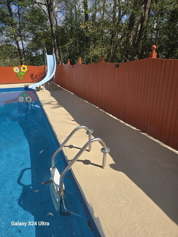 Textured pool deck surface with a handrail and pool ladder beside a swimming pool