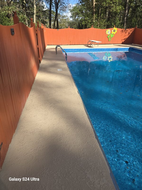 Resurfaced pool deck walkway running alongside a pool and privacy fence
