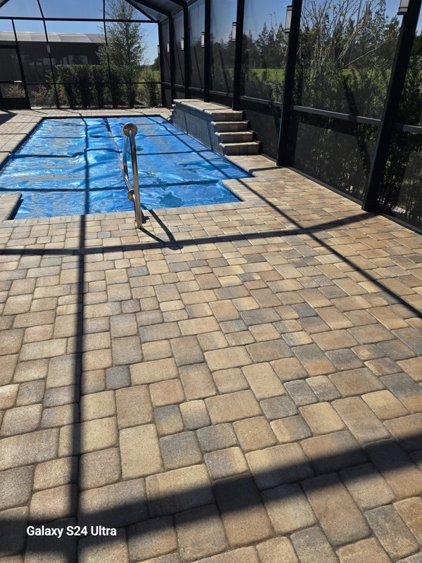 Paver pool deck inside a screened lanai with a covered pool and open lawn beyond