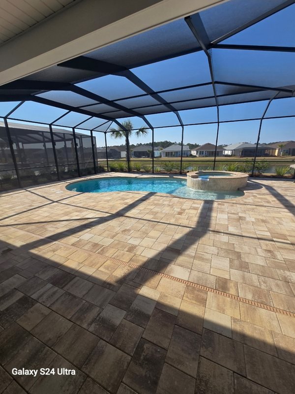Screened pool enclosure with a travertine paver deck and spa overlooking a pond