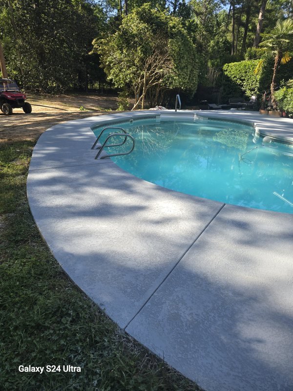 Broom-finished concrete pool deck curving around a backyard swimming pool