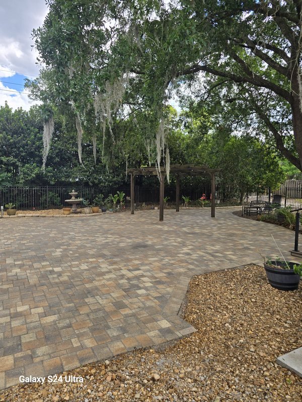 Shaded paver patio under mature oaks with a pergola and gravel border