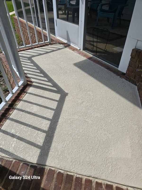 Textured concrete porch floor with a brick border alongside an enclosed sunroom