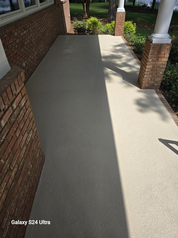 Smooth sealed concrete walkway between brick columns leading to a front entry