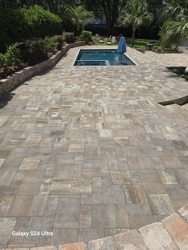 Multi-tone paver pool deck surrounding an in-ground pool with landscaped garden beds