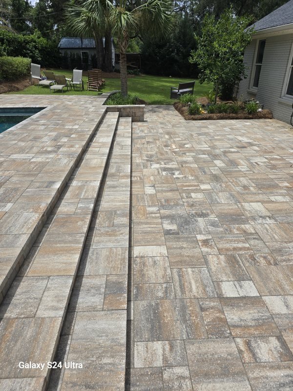 Wide paver patio with wraparound steps leading to a backyard pool and shaded seating area