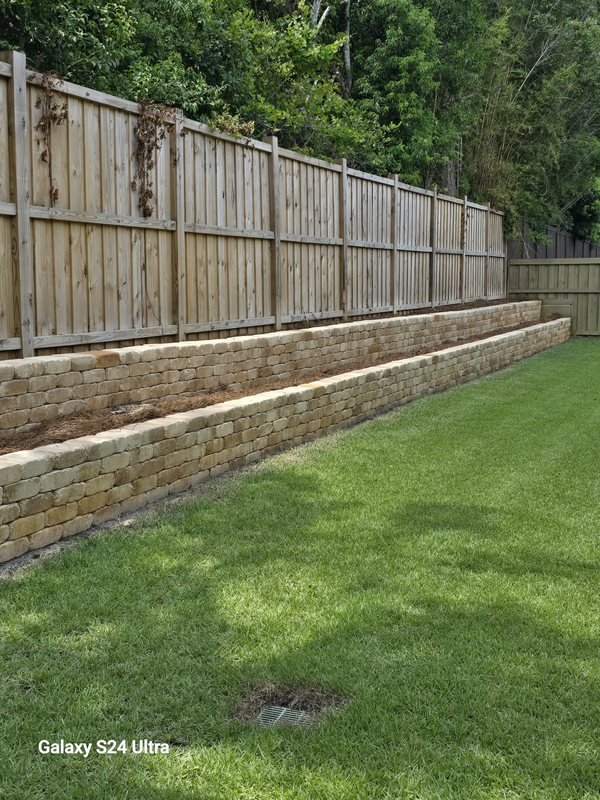 Paver retaining wall built along a wood privacy fence beside a manicured lawn