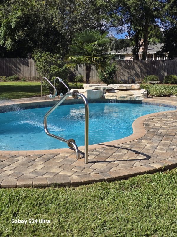 Curved paver walkway winding across a lawn toward a backyard swimming pool and fountain