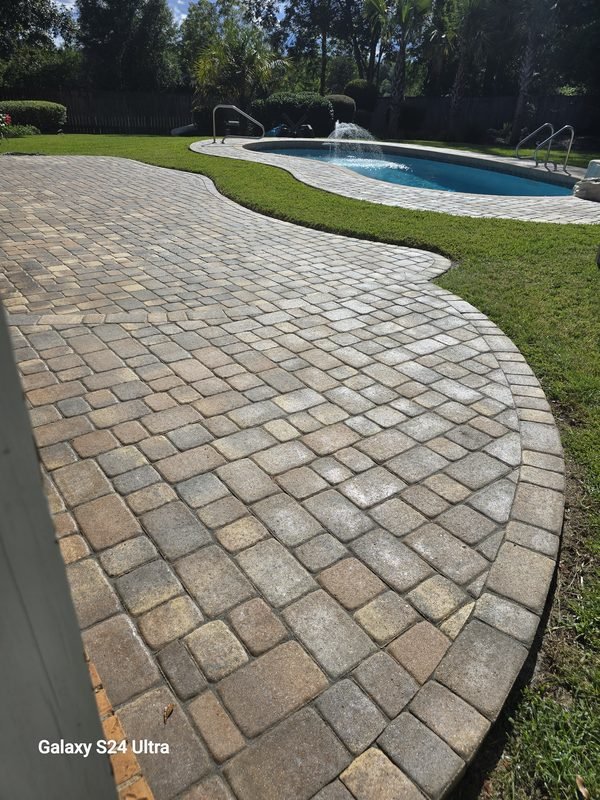 Free-form swimming pool with a stacked-stone water feature, ringed by a tan paver pool deck and green lawn